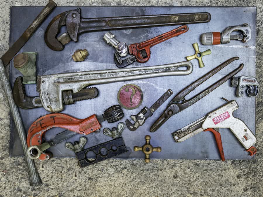 Plumbing wrenches and pipe tools laid out on a bench