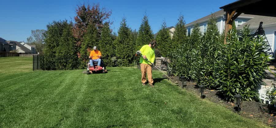 Two-person crew mowing and trimming a large lawn